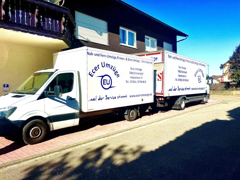 Zwei weiß beklebte Umzugslaster von Ecer Umzüge mit Firmenlogo und Kontaktdaten hintereinander am Straßenrand im Sonnenschein geparkt.