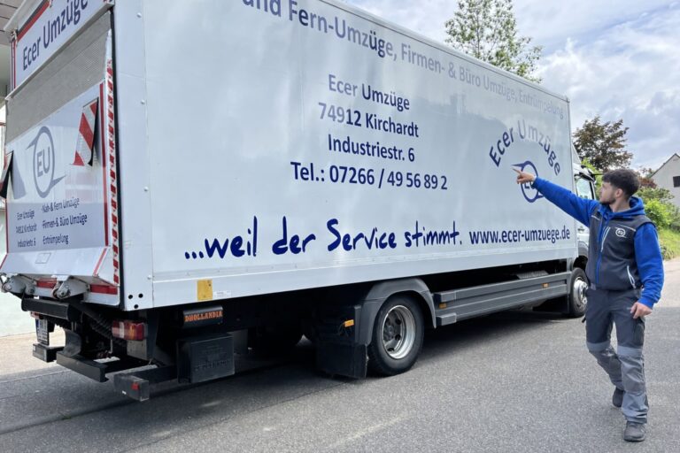 Seitenansicht eines Ecer-Umzüge-LKW mit gut sichtbarer Firmenaufschrift, Kontaktdaten und dem Slogan „…weil der Service stimmt“, rechts zeigt ein Mitarbeiterarm auf das Firmenlogo.