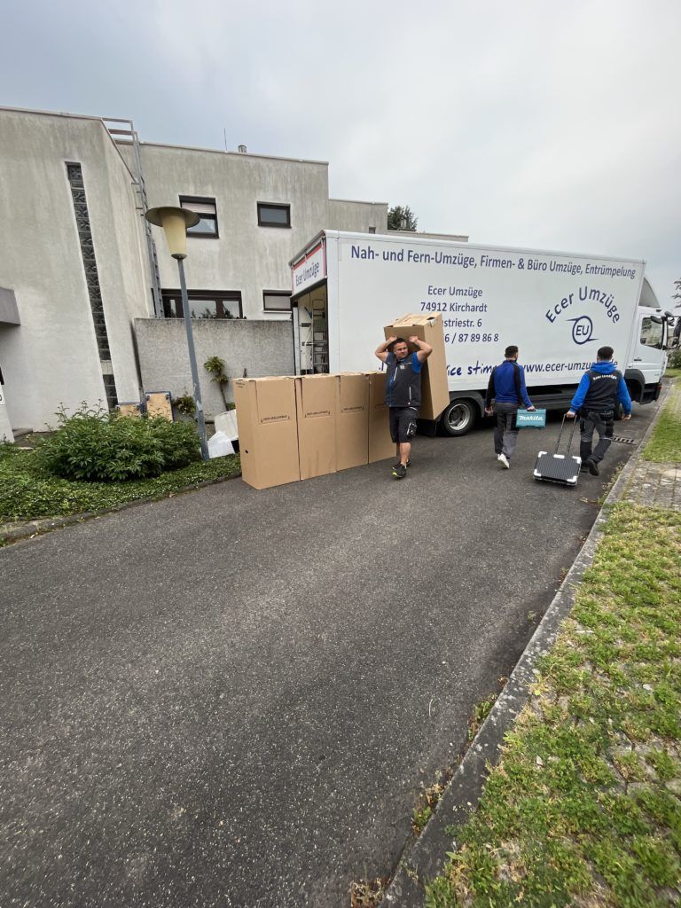 Umzugs-LKW von Ecer Umzüge vor einem Wohnhaus, davor ordentlich aufgereihte Umzugskartons und Umzugsequipment.